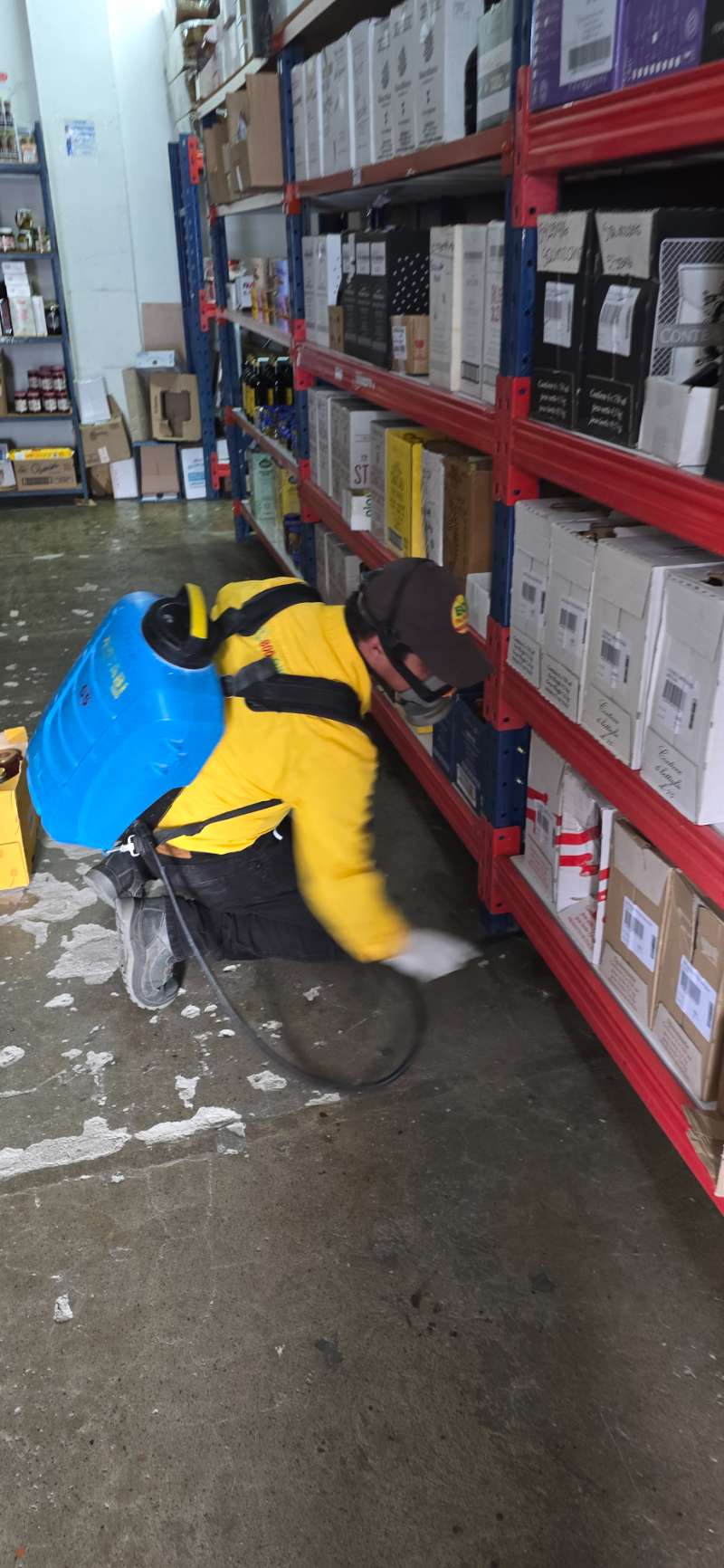 Técnico de EcoPlagas aplicando aspersión residual bajo estanterías de una bodega